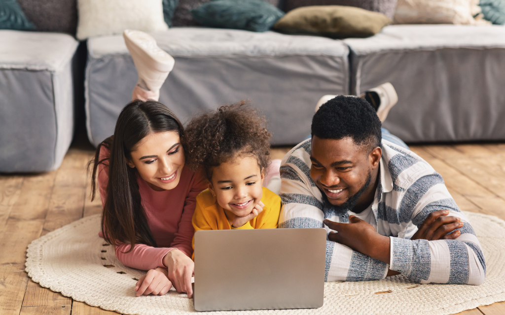 a family with a child watching video on a laptop on the floor