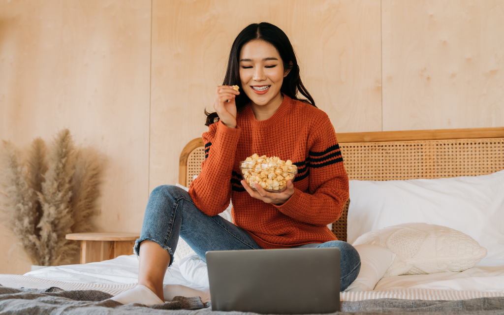 a woman eating popcorn and watching a moview on a laptop