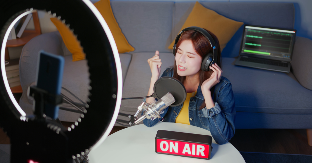 A young woman live streaming a podcast session from her home studio, complete with a ring light and professional equipment.