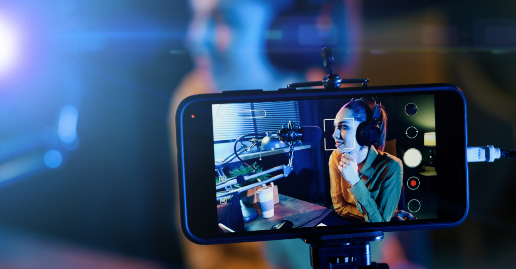 A content creator recording a live podcast with professional audio equipment, as seen through a smartphone screen.