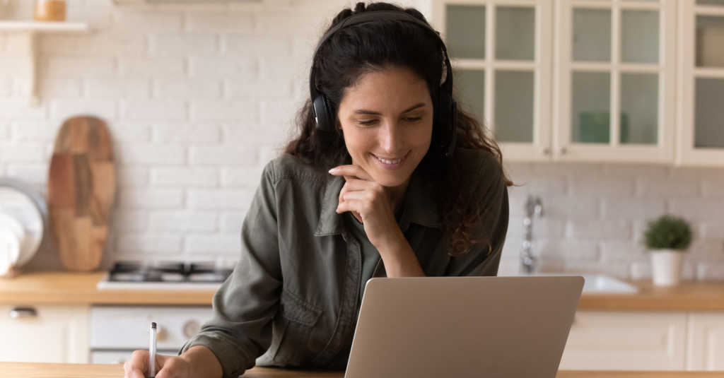 Woman with headphones watching a video on a laptop in the kitchen