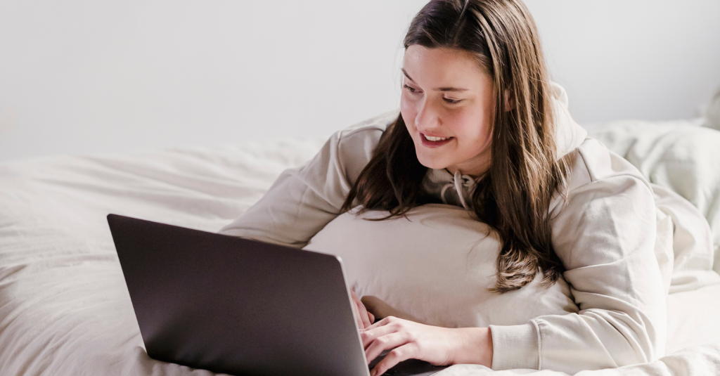 Young woman lying on a bed using a laptop for video streaming